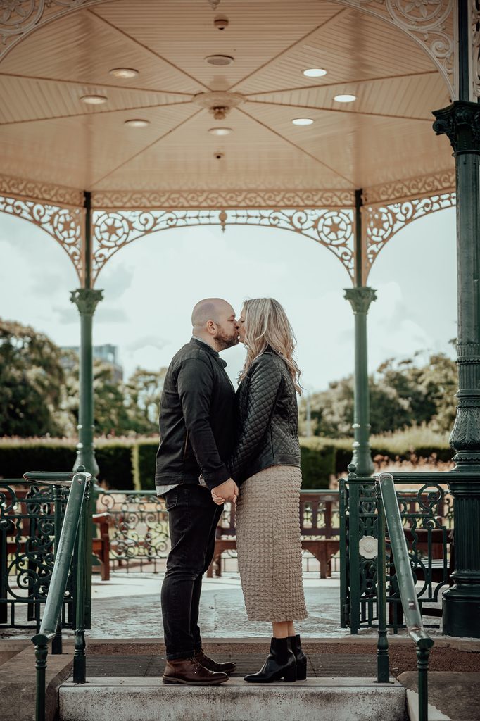 Engaged couple kissing beneath the bandstand at Saughton Park in Edinburgh