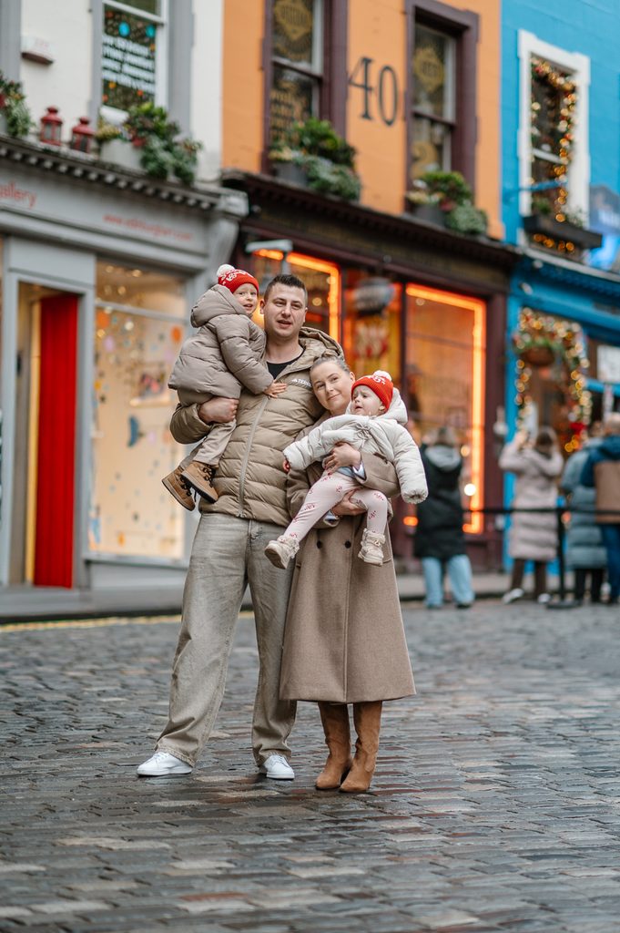 Parents holding their two young children on colourful Victoria Street during an Edinburgh vacation photoshoot