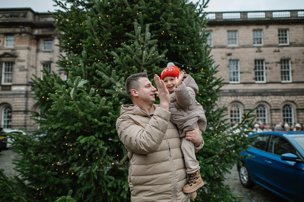Father and young child sharing a playful moment beside a Christmas tree in Edinburgh