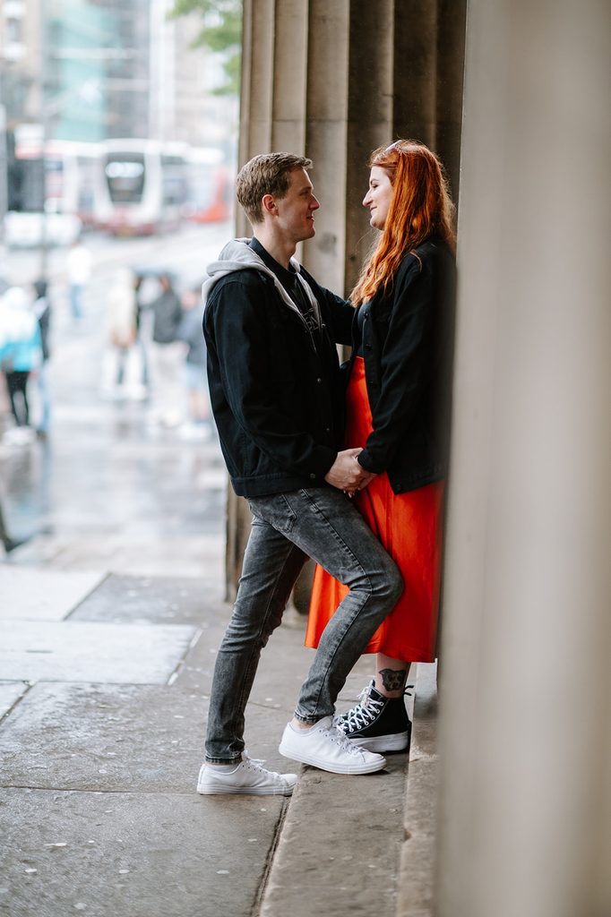 Laura and Fraser standing together beneath stone columns during their Edinburgh engagement photography session