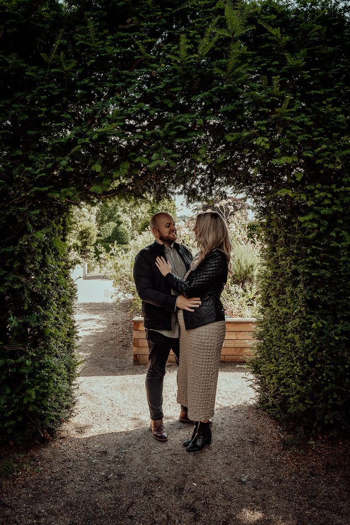 Natural engagement portrait of Jenna and Mike beneath a garden arch at Saughton Park