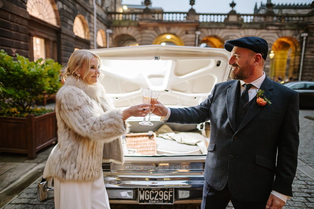 Steph and Keith raising a toast beside their vintage wedding car at Edinburgh City Chambers